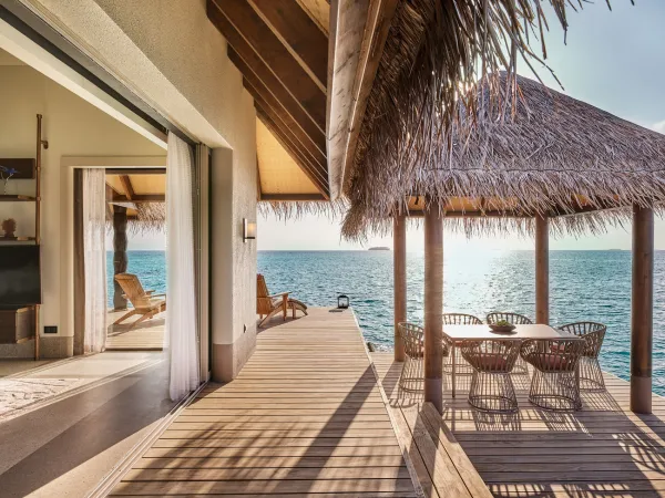 Over‑water dining table under thatched pavilion on sunny terrace, with panoramic ocean views at JOALI Maldives three‑bedroom