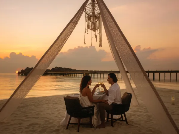 Couple embracing during a candlelit beach dinner on soft sand at JOALI Maldives at sunset.
