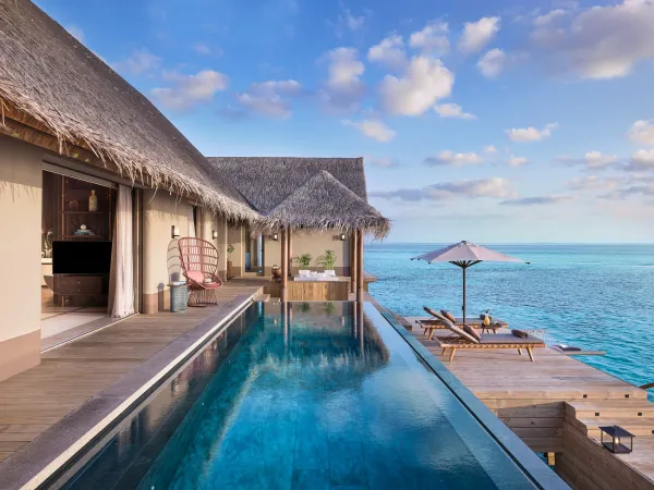 Overwater terrace with infinity pool, sun loungers and umbrella overlooking the Indian Ocean at JOALI Maldives Three‑Bedroom