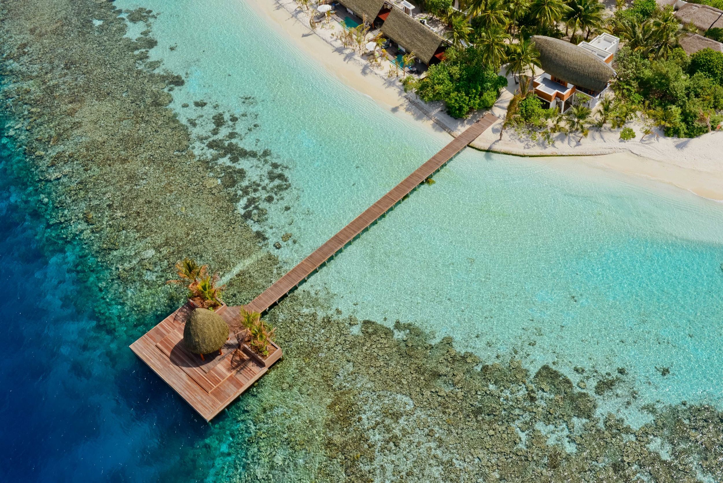 Aerial view of Kandolhu Maldives featuring overwater deck, coral reef, and beachfront villas surrounded by turquoise lagoon
