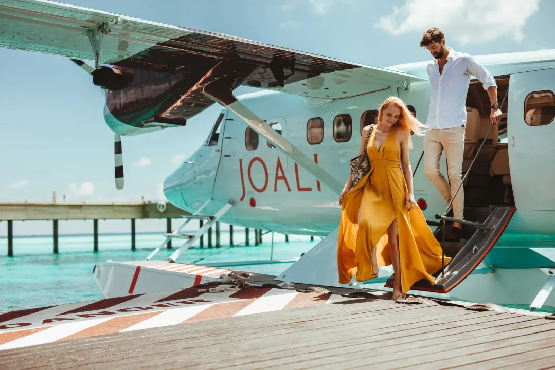 Couple arriving at Joali Maldives by private seaplane – luxury island welcome over turquoise waters and sunny tropical skies.