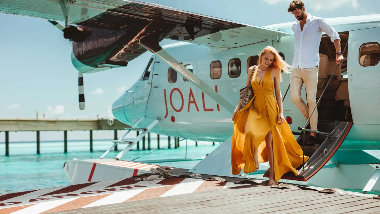 Couple arriving at Joali Maldives by private seaplane – luxury island welcome over turquoise waters and sunny tropical skies.