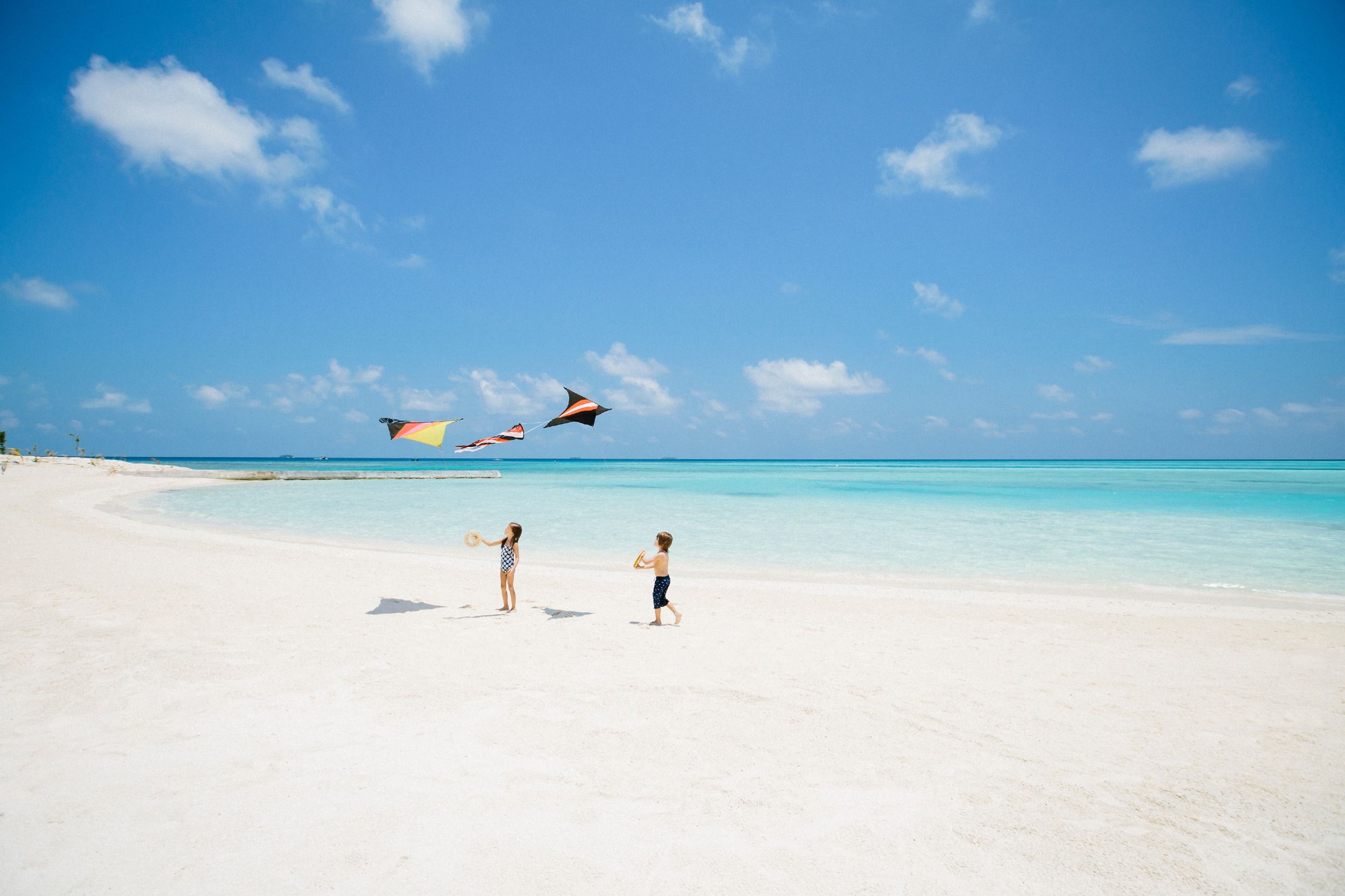 Children play with kites on a pristine white beach.