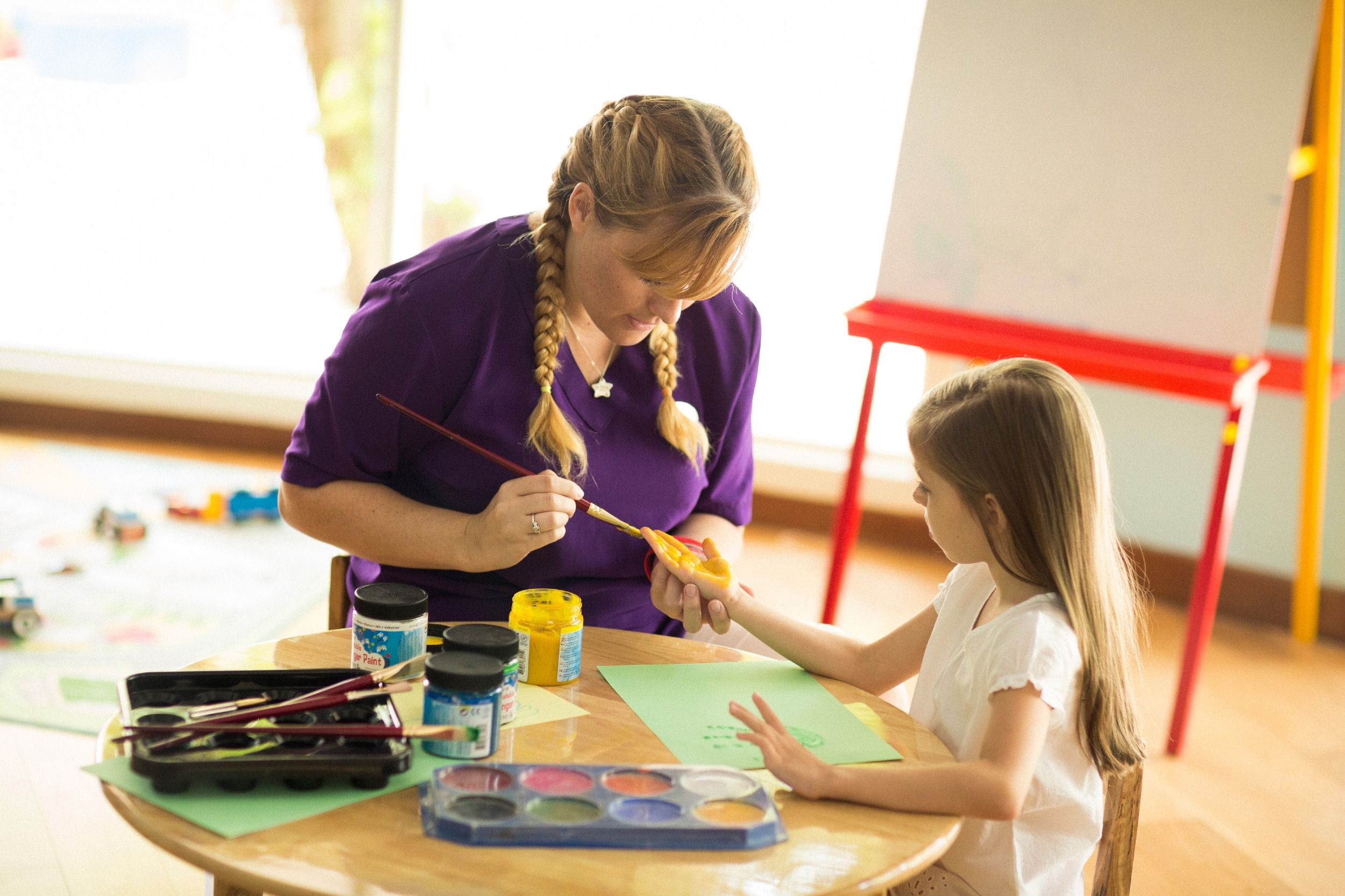 A staff member assists a young girl during painting at Explorers Kids Club. 